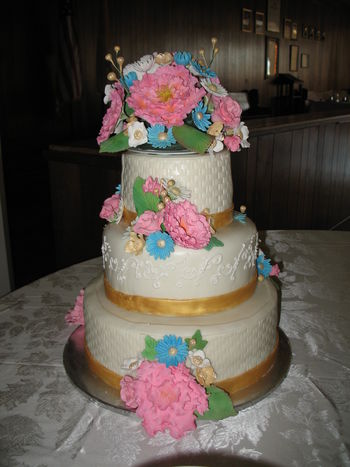 My second real wedding cake.  All tiers have RLB's silk meringue buttercream under MMF.  6" top tier was lemon ginger cake with lemon SMBC filling; 9" second tier was pumpkin spice cake with maple SMBC filling; 12" base tier was chocolate cake with chocolate Swiss meringue buttercream filling.  Royal icing piping on second tier and gumpaste peonies, blue and white daisies, fantasy flowers, gold buds, and pink roses.  For Cake Club to review.
