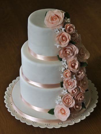 A three-tier birthday cake with sugarpaste roses and filler flowers cascading down the side.